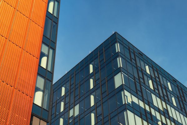 Modern office building exterior with glass facade on clear sky background. Transparent glass wall of office building with orange decoration. Element of facade of modern European building Commercial office buildings. Abstract modern business architecture