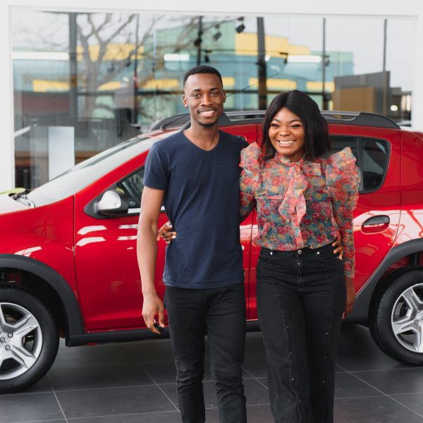 Smiling African American couple hugging and smiling at camera at new car showroom