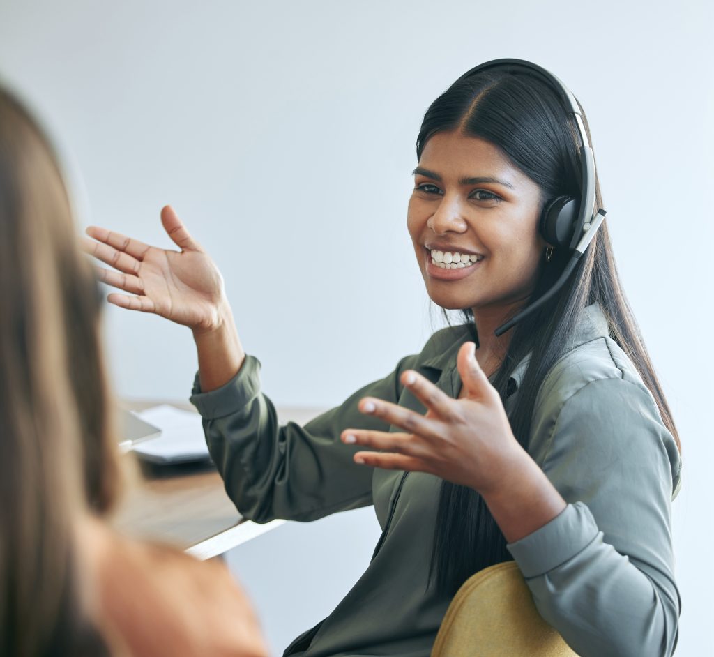 Shot of an attractive young saleswoman sitting in the office with a colleague and wearing a headset.