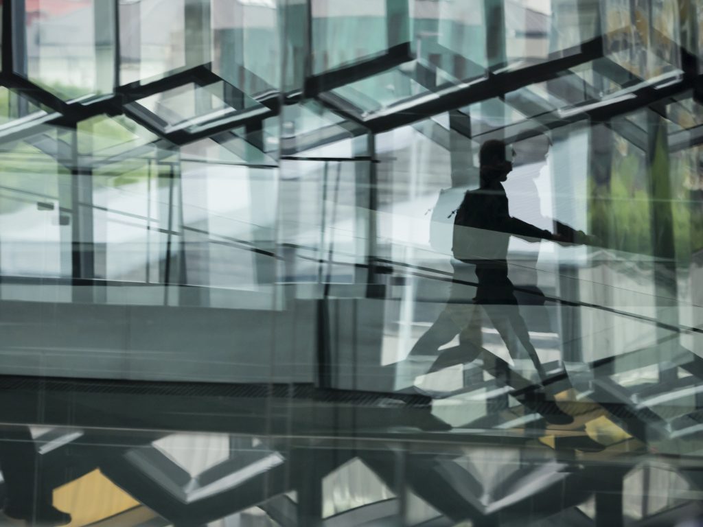 A man walking through the Harpa building, with glass walls and reflected light.